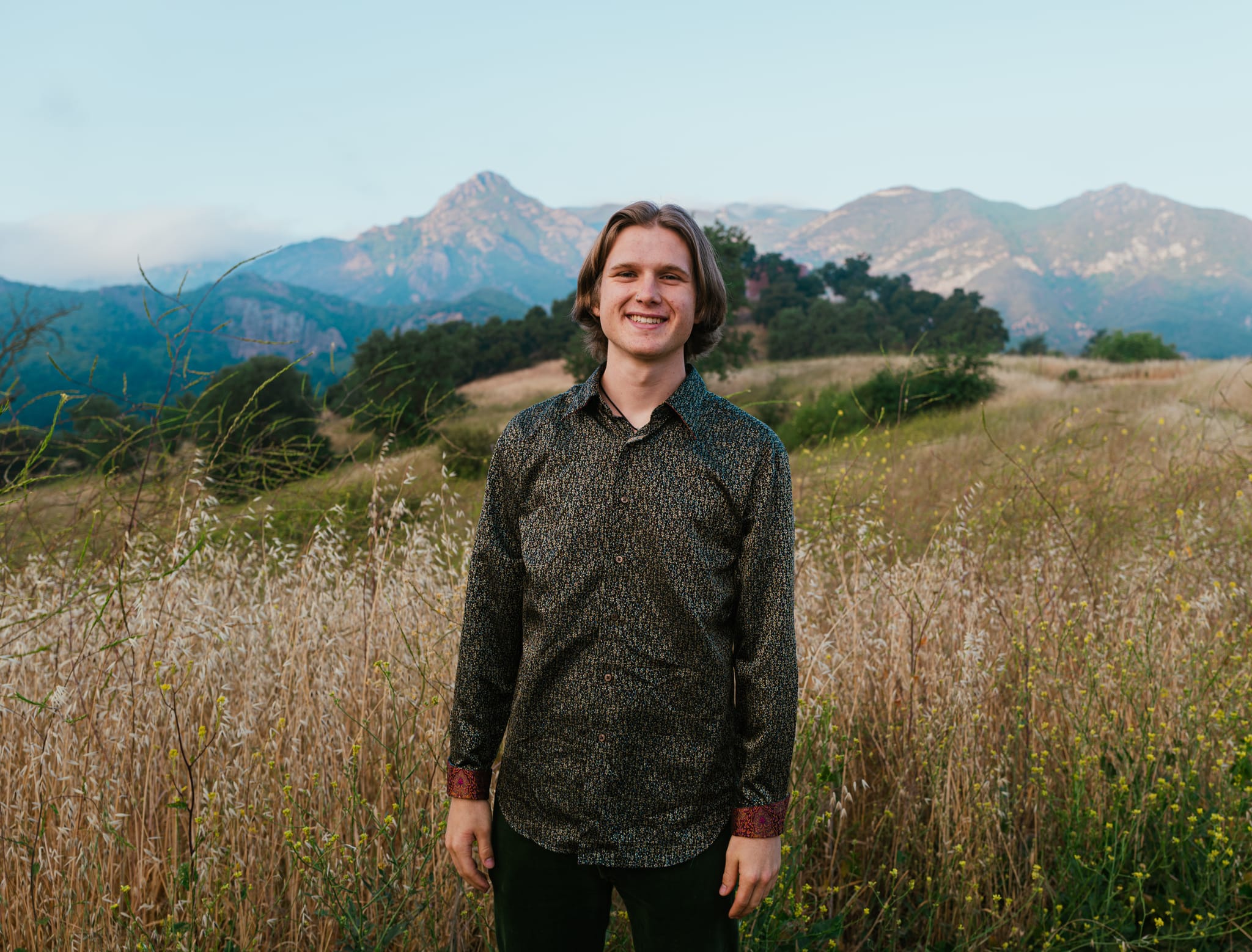 Abe standing in a field of tall golden grass with mountains behind him at Malibu Creek State Park